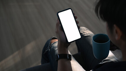 Cropped shot man holding empty screen mobile phone and coffee cup with sitting on sofa.