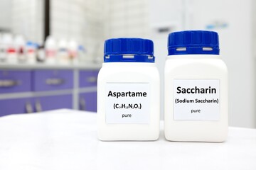 Selective focus of a bottle of pure aspartame and saccharin artificial sweetener sugar substitute chemical compound comparison. White laboratory background with copy space.