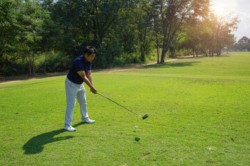 Fototapeta premium Golfer playing golf in the evening golf course, on sun set evening time. Man playing golf on a golf course in the sun.