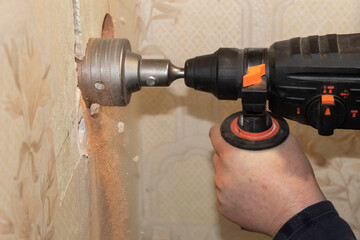 A man's hand drills holes in the wall for electrical outlets with a drill with a special nozzle.