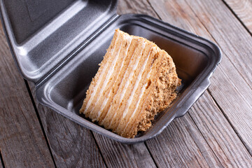 A piece of honey cake Medovik in container on a table.