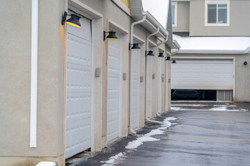 Garage doors and wall lamps of apartments along wet and snowy road in winter