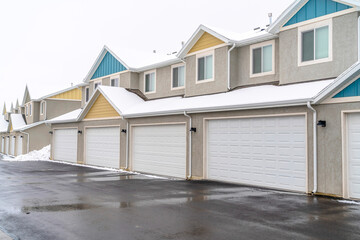 Homes with white garage doors along wet and snowy road on a cloudy winter day