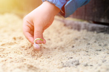 a kids hand planting a sprouted seed of garlic in a garden bed with sand in spring. flare