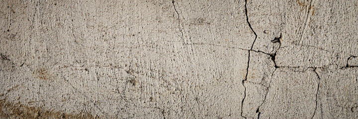 Concrete wall texture with cracked plaster. Weathered rough surface. Panoramic background for grunge design.