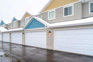 Back view of apartments with white garage doors and snowy roofs in winter