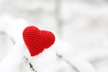 Valentine heart in winter forest, cold weather. Red knitted heart on snow covered branch, symbol of romantic love, background for holiday