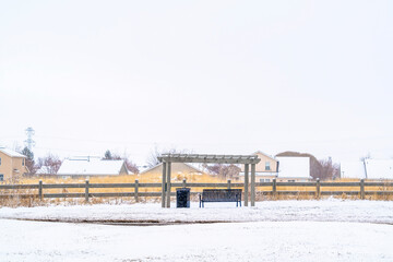 Fototapeta na wymiar Snowy landscape in winter with bench under pergola against vast overcast sky