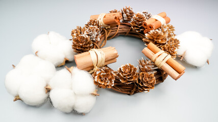 Beautiful hand made Christmas wooden wreath decorated with a bow, cinnamon and pine cones on gray background.