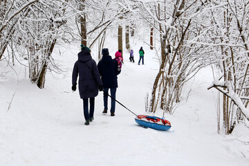 Family leisure in winter park, parents and a child with snow tube. People walking in frosty day
