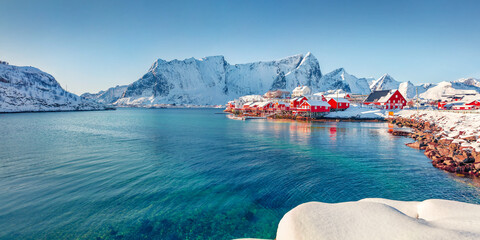 Panormic winter view of popular tourist destination - Lofoten Islands. Red houses on the shore of Norwegian sea. Sunny winter view of Sakrisoy fishing village.  Landscape photography.. - obrazy, fototapety, plakaty