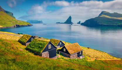 Beautiful summer scenery. Икшпре summer scene of Bour village with typical turf-top houses and Tindholmur cliffs on background. Attractive morning view of Vagar island, Faroe, Denmark, Europe.