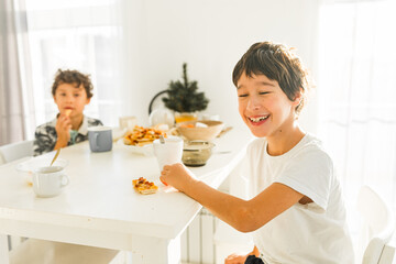 Obraz na płótnie Canvas Portrait of smiling boys having breakfast at home two real siblings
