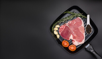 Raw T-bone Steak with fresh herbs and garlic, tomato, black pepper, rosemary on dark black background with copy space for your design, food concept. Top view.