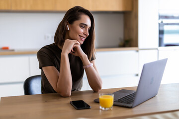 Woman works from home. An employee sits in kitchen and has a lot of work on laptop at video conferencing and meetings uses headphones with a headset.