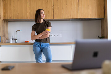 Attractive young woman holding a glass of orange juice while standing in the kitchen