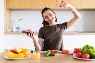 Cheerful woman prepare ecological fresh veggie supper enjoy listen headset music dance dancer in kitchen