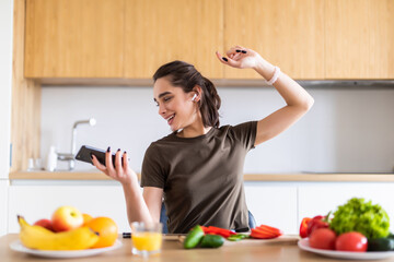 Young woman listening to music and dancing while cooking in kitchen