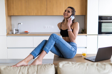 Cheerful young woman talking on the phone in the kitchen