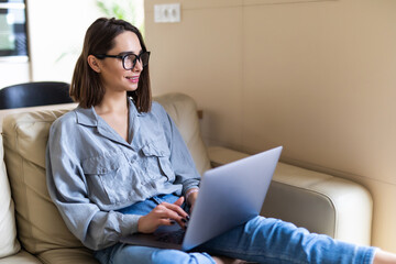 Happy pretty woman using laptop sitting on cosy sofa