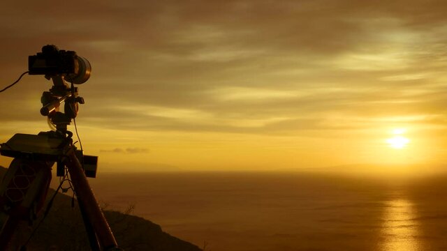 Professional camera on tripod taking picture film video of sunrise over sea water, Greece Peloponnese Mani Peninsula. Time lapse