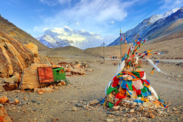 View of stone formation covered by colorful praying flags near the RongPu Monastery, against a blue sky above Mount Everest.