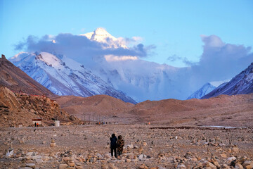 Tourists admiring Mount Everest at the Everest Base Camp in Tibet, against a blue sky covered by white clouds.