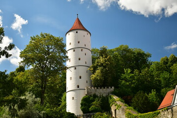 Ein weißer Turm samt Stadtmauer zwischen alten Bäumen