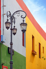 Vertical view of a street lamp and colorful buildings of the Argentinean district La Boca, in Buenos Aires, with old walls against a blue sky.
