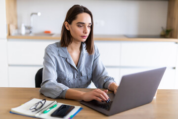 Young beautiful woman works on laptop from a home on a desk as a freelancer