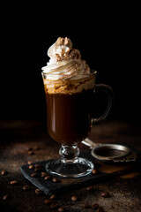 Black hot arabica coffee with cream and cinnamon in a glass glass on a dark