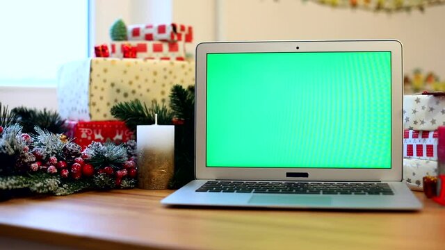 Green screen notebook with Christmas decoration on background. Presents for family. Chroma-key laptop. Free content. Mockup monitor. Online greeting. Internet surfing. New Year Celebrating concept.