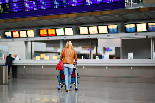 Female travel tourist pushing trolley with luggage at airport terminal. Unrecognizable faceless woman going to airline check in or boarding and waiting for her plane. Travel lifestyle.