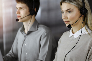 Diverse people group in sunny call center. Blonde business woman talking by headset while sitting...