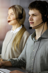 Businessman talking by headset while sitting in sunny office. Telemarketing concept - 402809567