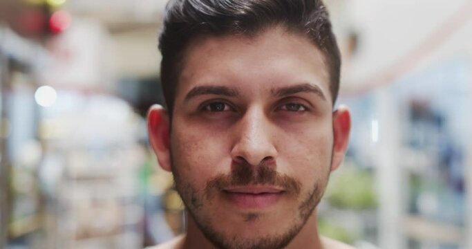 Young Brazilian man smiling in a marketplace. Latin man smiling to camera. 4K.