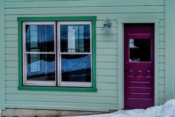 Fototapeta na wymiar Glass paned purple front door and single hung windows at facade of green home