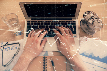 Double exposure of man's hands typing over laptop keyboard and forex chart hologram drawing. Top view. Financial markets concept.