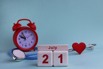 July 21. White wooden calendar blocks with date, clock and stethoscope on blue pastel background....
