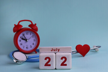 July 22. White wooden calendar blocks with date, clock and stethoscope on blue pastel background. Selective focus. health concept