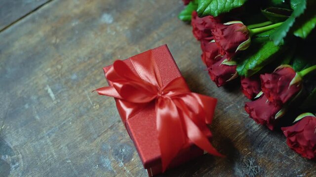 red box with a satin bow on a wooden background, a bouquet of beautiful red roses. gift concept for valentine's day, birthday, anniversary,