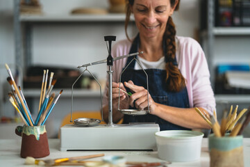 Happy woman pouring paint colors powder on vintage balance in pottery studio - Focus on balance