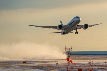 小雪舞う空港を雪煙を上げながら離陸する航空機