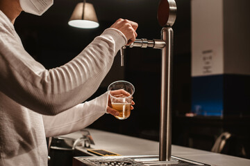 Camarero vertiendo cerveza fresca del grifo en un vaso de plástico en un bar por la noche mientras...