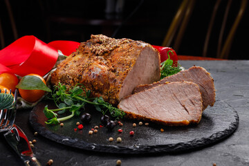 a piece of baked pork with spices on a black plate and a dark background.