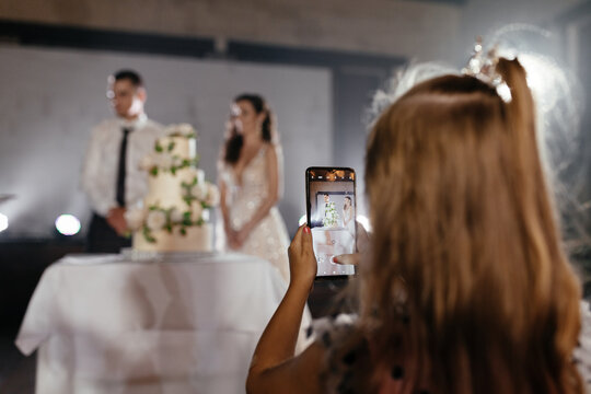 Little girl taking a picture of newlyweds and cake on the smartphone. Place for your text. Wedding background
