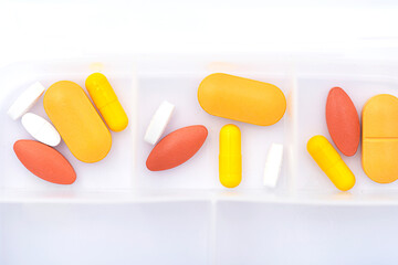 Opened pill box with yellow, red pills on white table