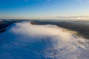 Aerial drone view of snow covered mountains and towns rising above the south east valleys, Wales