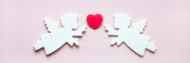 Romantic composition of two white felt angels and red heart on a powder pink background. Website banner. Concept of love, St. Valentines day, wedding and other holidays.