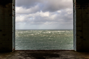 Window frame in derelict building looking out to stormy sea.